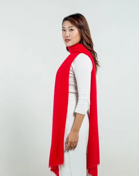 woman in a bright red cashmere scarf draped over a white outfit, showcasing its style. 